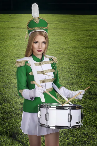 Beautiful blonde cheerleader drummer with drum on the background of green grass — Stock Photo, Image