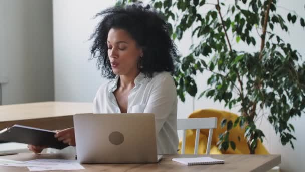 Ritratto di una giovane donna afroamericana che parla in videoconferenza con laptop e auricolare, mostrando grafici. Bruna si siede a tavola in luce home office. Chiudete. Rallentatore pronto 59.97 fps. — Video Stock