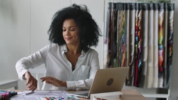 Retrato de una joven afroamericana mirando a través de la paleta de colores y muestras de telas para el proyecto de diseño. La diseñadora se sienta a la mesa en la oficina. De cerca. Cámara lenta lista 59.97fps. — Vídeos de Stock