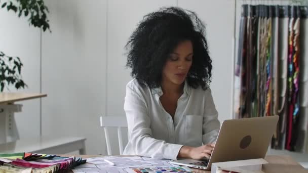 Porträtt av ung afroamerikansk kvinna som tittar igenom färgpalett och prover av tyger för designprojekt. Kvinnlig designer sitter vid bordet på kontoret. Närbild. Slow motion klar 59,97fps. — Stockvideo