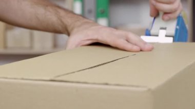 Genç bir erkek mağaza sahibi, depo çalışanı, kaset paketli tüccar fişleri teslimat karton kutu hazırlıyor. Eller yukarı. Posta servisi. Yavaş çekim hazır 59.94fps.