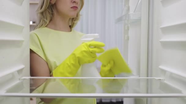 Vista desde el interior de un refrigerador vacío mientras se limpia. Mujer joven en guantes de goma lava nevera con una botella de spray y un trapo, hacer las tareas domésticas. De cerca. Cámara lenta lista 59.94fps. — Vídeos de Stock