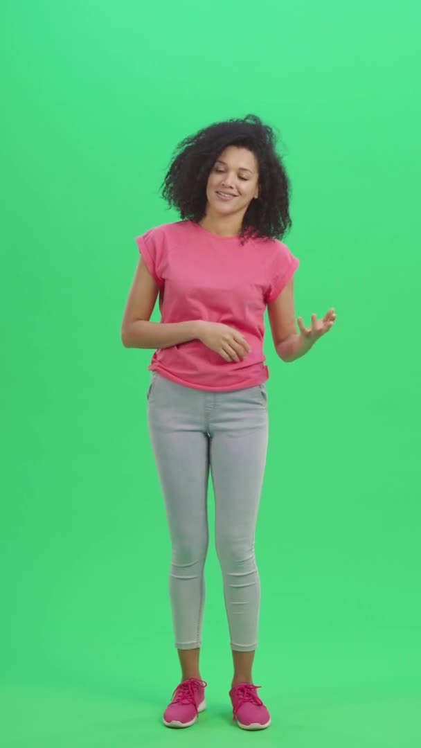 Portrait of young female African American waving hello and communicating with someone in friendly way. Black woman with curly hair poses on green screen. Slow motion ready 59.97fps. Full length. — Stock Video