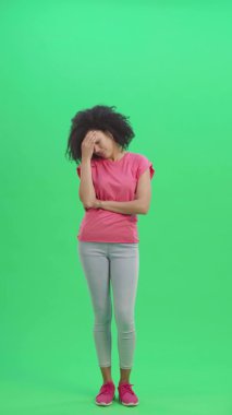 Yorgunluktan muzdarip genç Afrikalı Amerikalı kadın portresi. Kıvırcık saçlı siyah kadın stüdyoda yeşil ekranda poz veriyor. Yavaş çekim hazır 59.97 fp. Dikey video. Tam uzunluk