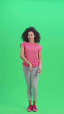 Genç Afro-Amerikan kadın portresi bir şey için işaret ediyor sonra başını sallıyor ve başparmağını gösteriyor. Siyah kadın yeşil ekranda poz veriyor. Yavaş çekim hazır 59.97 fp. Dikey video. Tam uzunluk.