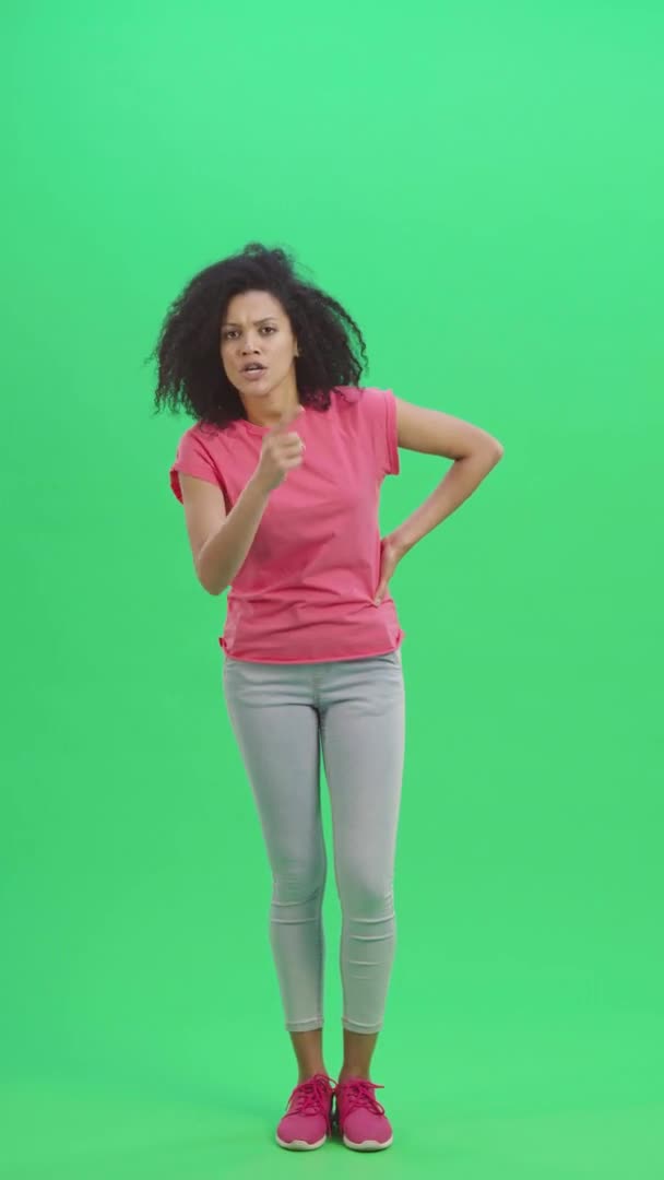 Portrait of young female African American swears and shakes viciously with his index finger. Black woman with curly hair poses on green screen. Slow motion ready 59.97fps. Vertical video. Full length. — Stock Video