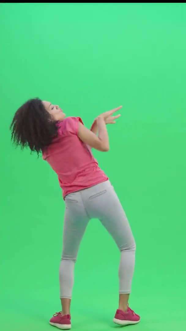 Портрет молодой женщины-афроамериканки, весело танцующей танец победы, радости или хорошего настроения. Черная женщина позирует на зеленом экране. Slow motion ready 59.97fps. Вертикальное видео. Полная длина. — стоковое видео