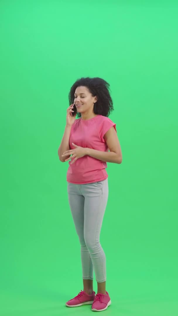 Porträtt av ung kvinna afroamerikan talar för mobiltelefon och glädjas. Svart kvinna med lockigt hår poserar på grön skärm i studion. Slow motion klar 59,97fps. fp. Vertikal video. Full längd — Stockvideo
