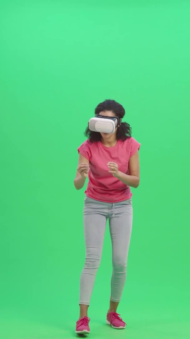 Retrato de una joven afroamericana con auriculares de realidad virtual o gafas 3D. Mujer negra con pelo rizado posa en la pantalla verde. Cámara lenta lista 59.97 fps. Vídeo vertical. Longitud completa. — Vídeos de Stock