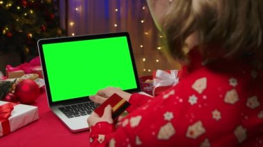 Yeşil ekran krom anahtarı olan kredi kartı ve laptop kullanan bir kadın. Noel evi hediyeler, köknar ağacı ve ışıklarla dolu. Yeni yıl tatili konsepti. Kapatın. Yavaş çekim.