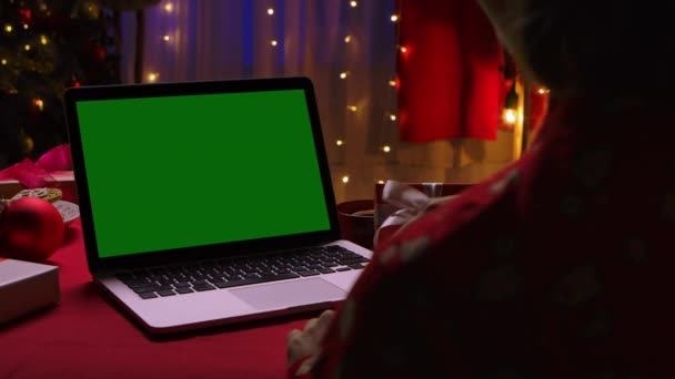 Widok z tyłu kobiety na laptopie z zielonym ekranem chroma klucz na tle wnętrza domu urządzone na Sylwestra. Komunikacja online przez czat wideo. Zamknij drzwi. Zwolniony ruch. — Wideo stockowe
