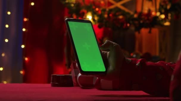 Woman uses a smartphone to view content, communicate in social networks. Christmas interior decorations in red colors. Close up female hands touch the phone with a green screen chroma key. Slow motion — Stock Video