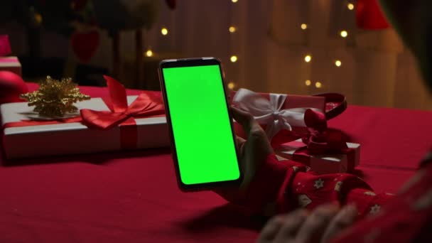 Женщина держит в руке смартфон с зеленым цветовым ключом на фоне домашнего интерьера, украшенного в канун Нового года. Онлайн-общение через видео чат. Закрывай. Медленное движение. — стоковое видео