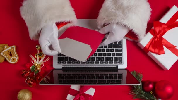 Noel Baba 'nın elleri beyaz eldivenlerle kırmızı yeni yıl süsleme masasında klavye bilgisayarında daktilo ediyor. Noel Baba çocuklardan gelen mektuplara bakar ve internetten hediyeler alır. Kapatın. Yavaş çekim. — Stok video