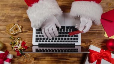 Noel Baba 'nın elleri beyaz eldivenlerle klavyeye ahşap yeni yıl süsleme masasıyla yazı yazıyor. Noel Baba internetten kredi kartıyla alışveriş yaparken dizüstü bilgisayarla çalışır. Kapatın. Yavaş çekim.