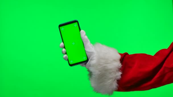 Santa Claus hands in white gloves hold a smartphone in a vertical position with a green screen chroma key. Isolated on a green background in the studio. Mock up display. Close up. Slow motion. — Stock Video