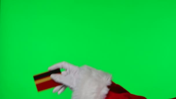 Руки Санта Клауса в красном костюме и белые перчатки держат банковскую карту. Изолирован на зеленом экране в студии. Хрома-ключ. Закрывай. Медленное движение. — стоковое видео