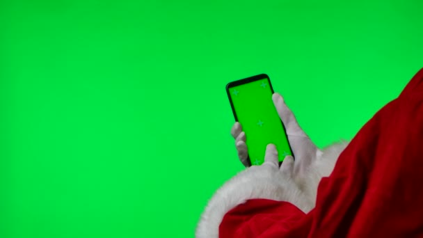 Santa Claus ruce v bílých rukavicích pomocí smartphonu, přejeďte a klepněte na zelený displej chroma klíč. Izolovaný na zeleném pozadí ve studiu. Zesměšňujte displej. Zavřít. Zpomalený pohyb. — Stock video