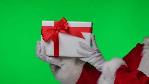 Vue latérale du Père Noël en gants blancs et un costume rouge fait tournoyer une boîte cadeau dans ses mains. Isolé sur un écran vert dans un studio. Clé chromatique. Ferme là. Mouvement lent. — Video