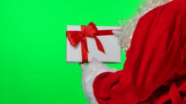 Beyaz eldivenli sakallı ve kırmızı elbiseli Noel Baba 'nın arkasından bir hediye kutusu fırıl fırıl dönüyor. Stüdyoda yeşil bir ekranda izole edilmiş. Krom anahtar. Kapatın. Yavaş çekim.