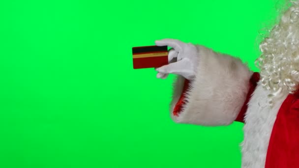 Zijaanzicht De Kerstman met een baard in witte handschoenen houdt een creditcard vast en wijst ernaar met zijn vinger. Afgezonderd op een groen scherm in de studio. Chroma sleutel. Sluit maar af. Langzame beweging. — Stockvideo