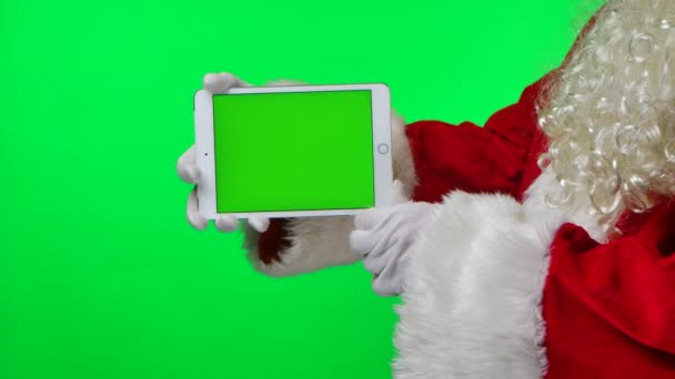 Boční pohled Santa Claus s plnovousem v bílých rukavicích drží tablet ve vodorovné poloze se zeleným displejem chroma klíčem. Izolované na zeleném pozadí ve studiu. Zesměšňujte displej. Zavřít. Zpomalený pohyb. — Stock video