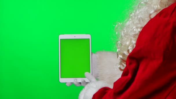 Side view Santa Claus with beard in white gloves hold tablet in vertical position and points finger with green screen chroma key. Isolated on green background in the studio. Close up. Slow motion. — Stock Video