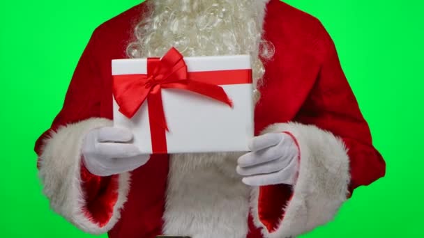 Santa Claus with beard in white gloves and a red suit holding a gift box in his hands. Isolated on a green screen in a studio. Chroma key. Close up. Slow motion. — Stock Video