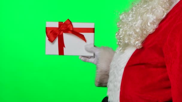 Vista lateral de Santa Claus con barba en guantes blancos y un traje rojo gira una caja de regalo en sus manos. Aislado en una pantalla verde en un estudio. Clave de croma. De cerca. Movimiento lento. — Vídeos de Stock