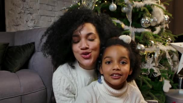 Πορτρέτο της χαρούμενης Αφρο-Αμερικανίδας μαμάς και κόρης που εύχονται Καλά Χριστούγεννα και Ευτυχισμένο το Νέο Έτος. Οικογένεια στο φόντο ενός διακοσμημένου χριστουγεννιάτικου δέντρου στο σπίτι. Κλείσε. Αργή κίνηση. — Αρχείο Βίντεο