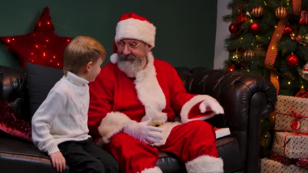 Noel Baba küçük bir çocuğa sevgi dolu bir hediye verir, çocuk sevinir ve sihirli büyükbabasına sarılır. Tatiller ve kutlamalar. Mutlu Noel arifeleri. Kapatın. Yavaş çekim. — Stok video