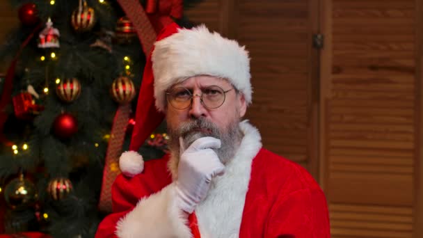 Retrato de Papai Noel olhando para a câmera escuta atentamente e faz um gesto ok. Homem velho em terno vermelho e chapéu contra o fundo da árvore de Natal com brinquedos e luzes. Ver captura de tela: Fecha. Movimento lento. — Vídeo de Stock