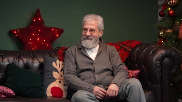 Lindo niño pequeño sorprendió a su abuelo con un regalo impresionante para la víspera de Navidad. Un abuelo anciano abraza a su nieto en una habitación decorada cerca de un árbol de Navidad brillante. Movimiento lento. — Vídeo de stock