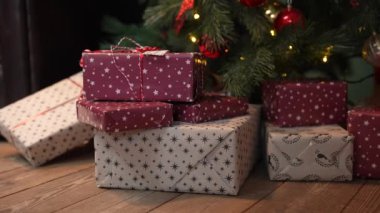 Noel 'in güzel hediye kutuları bir yığın hediyeyle ağacın altında, ahşap zeminde yatıyor. Yeni yıl hediyeleri, festival ve tatil alışverişi. Noel tebrik kartı. Kapatın. Yavaş çekim.