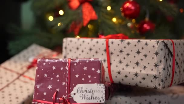 Gyönyörű ajándékdobozok fekszenek közel a karácsonyfa díszített ragyogó koszorú és golyók. Újévi háttér ajándékdobozzal. A karácsonyt ünnepeljük. Ünnepi hangulat. Közelről. Lassú mozgás.. — Stock videók