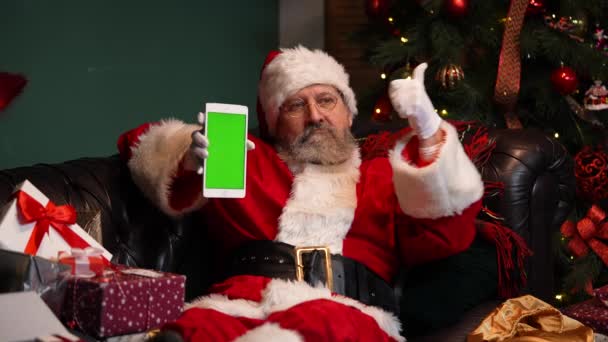 Mikulás fekszik a kanapén, közel egy díszített karácsonyfa, és azt mutatja, egy tabletta egy zöld képernyő króm kulcs, miközben egy hüvelykujj fel gesztus. Újévi reklám, előléptetés. Közelről. Lassú mozgás..