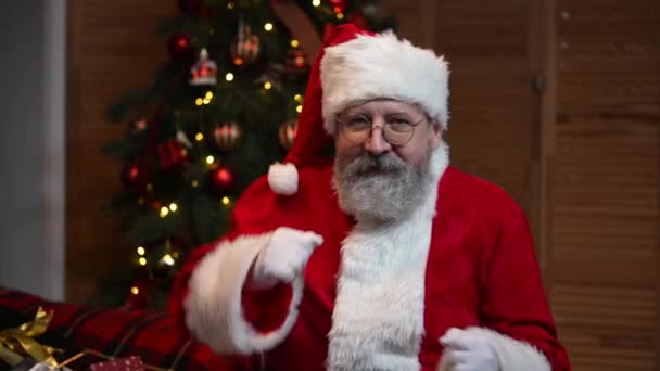 Портрет Санта Клауса танцует смешно. Старик с бородой в красном костюме и шляпе на фоне рождественской елки с игрушками и огнями. Счастливого Нового Года. Медленное движение. — стоковое видео