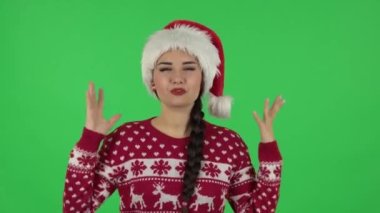 Noel Baba şapkalı tatlı kızın portresi konuşuyor ve bir şeyi işaret ediyor, kopyalama alanı. Yeşil Ekran