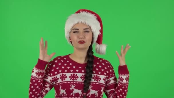 Porträtt av söt flicka i jultomten hatt talar och pekar sida hand för något, kopiera utrymme. Grön skärm — Stockvideo