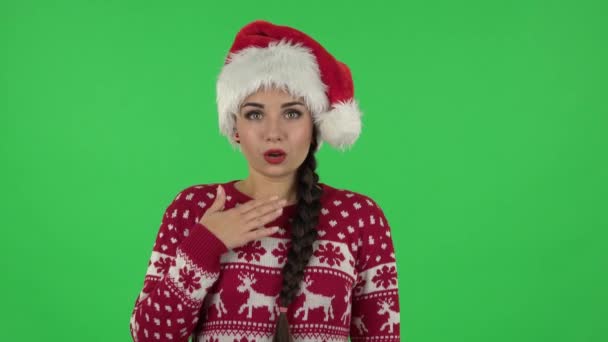 Портрет милой девушки в шляпе Санта Клауса говорит упс и пожимает плечами и кусает губы. Зеленый экран — стоковое видео