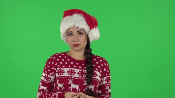 Портрет милой девушки в шляпе Санта-Клауса в предвкушении волнений, а затем виновный прячет глаза. Зеленый экран — стоковое видео