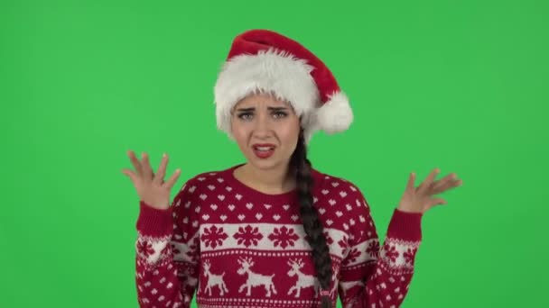 Портрет милой девушки в шляпе Санта-Клауса расстроен, машет руками в негодовании, пожимает плечами. Зеленый экран — стоковое видео