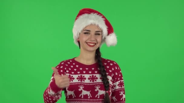 Portret słodkiej dziewczyny w czapce Świętego Mikołaja pokazuje kciuki do góry, gest jak. Zielony ekran — Wideo stockowe