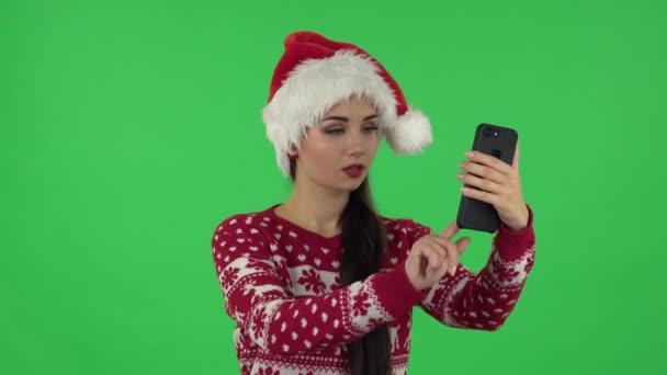 Портрет милой девушки в шляпе Санта-Клауса говорит для видео-чата с помощью мобильного телефона. Зеленый экран — стоковое видео