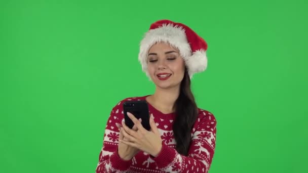 Porträt von Sweety Girl mit Weihnachtsmannmütze macht Selfie auf Handy dann Fotos suchen. Grüner Bildschirm