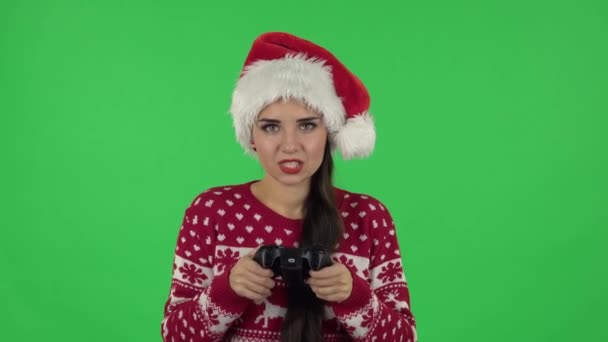 戴着圣诞老人帽子的女主角正在用无线控制器玩电子游戏，并为胜利而欢欣鼓舞。绿屏 — 图库视频影像