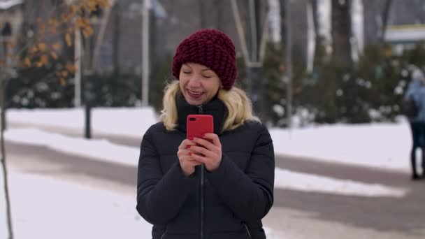 一个微笑着在电话上留言的女人的画像。女孩在雪地覆盖的街道的模糊的背景上和路过的过路人摆姿势。慢动作靠近点. — 图库视频影像