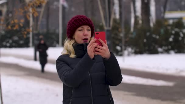 Portret szczęśliwej dziewczyny robiącej selfie na smartfonie na ulicy zimowego miasta. Nowoczesna technologia, styl życia i koncepcja radosnych ludzi. Zamknij drzwi. Zwolniony ruch. — Wideo stockowe