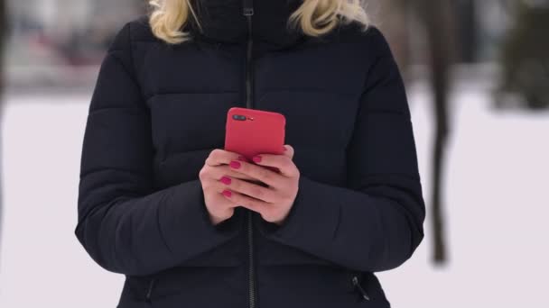 雪道を背景に、女性が携帯電話にテキストメッセージを書き込む。女の子の手の携帯電話にテキストメッセージを入力して閉じます。スローモーション. — ストック動画