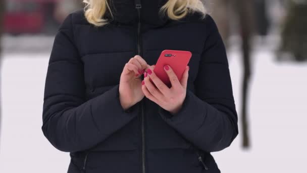 Una donna scrive un messaggio sul suo telefono su uno sfondo sfocato di una strada innevata. Primo piano di una mano ragazze digitando un messaggio di testo al telefono. Rallentatore. — Video Stock